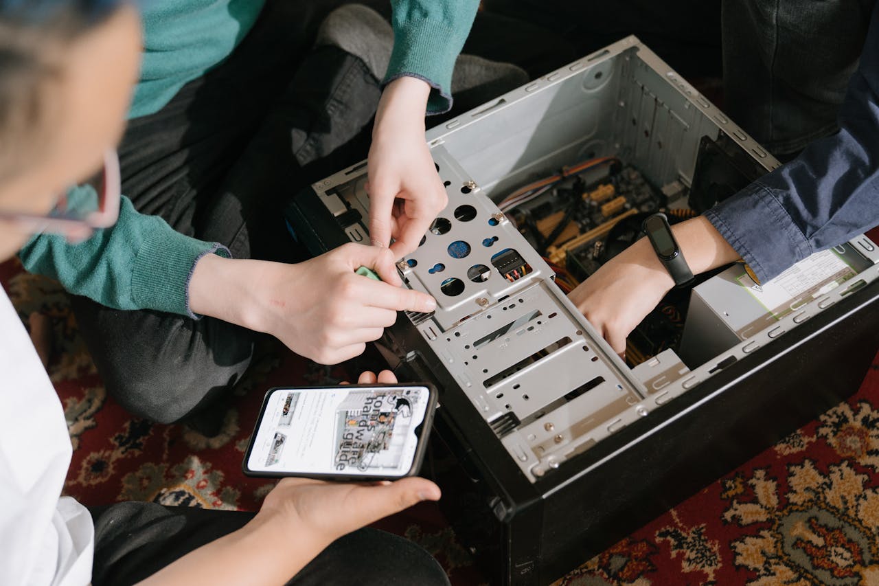 A close-up of hands fixing a computer with guidance from a mobile device.