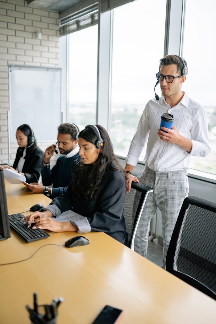 Diverse call center team working together in a modern office setting, using headsets and computers.
